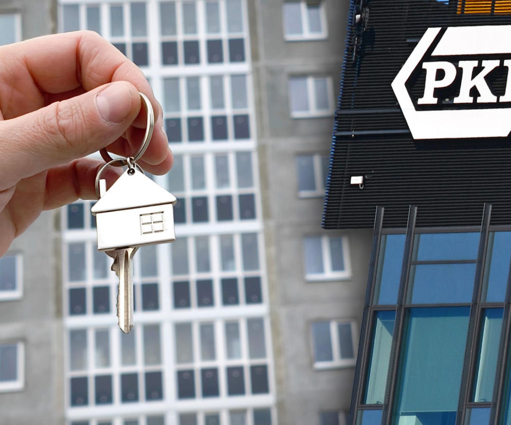 Dłoń trzyma klucz z brelokiem w kształcie domu, symbolizującym własność mieszkania. W tle widać nowoczesny budynek z logo PKP oraz blok mieszkalny. Zdjęcie ilustruje temat sprzedaży nieruchomości przez PKP, o czym przeczytasz na Super Biznes.