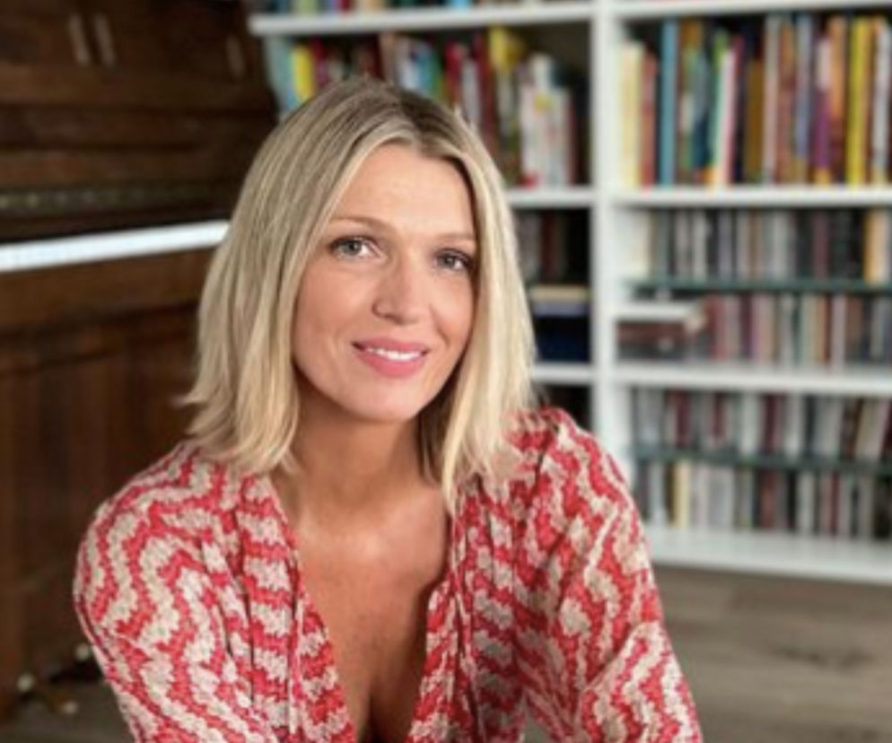 Magda Mołek z promiennym uśmiechem, w kwiecistej bluzce, siedząca na tle pianina i regału z książkami. Dziennikarka opowiada o swojej walce z Hashimoto. Więcej o chorobach przewlekłych i zdrowiu można przeczytać na portalu Poradnik Zdrowie.