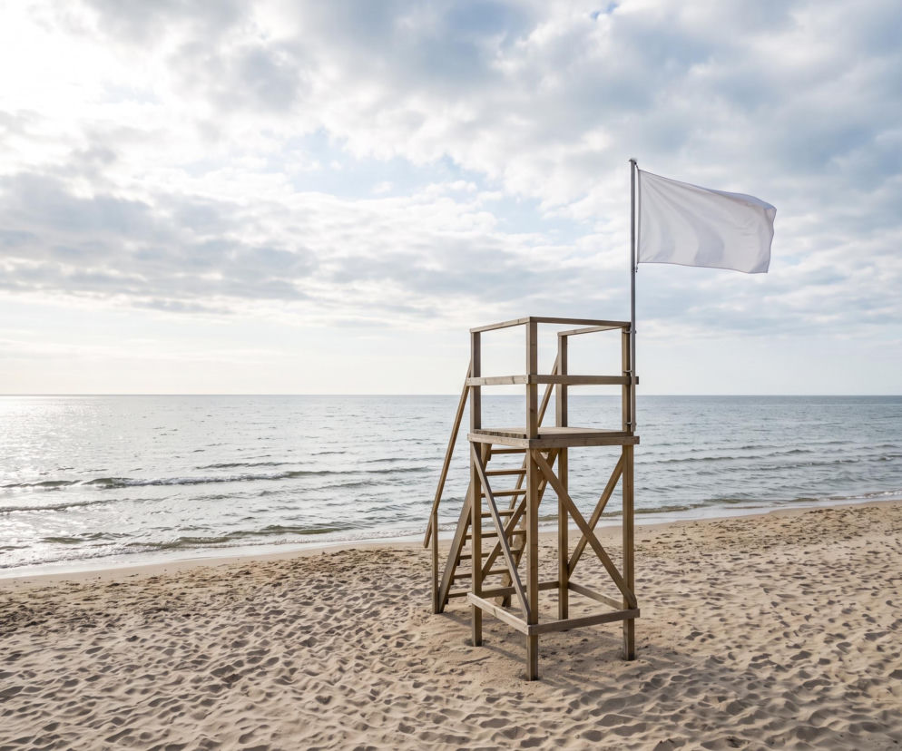 Drewniana wieża ratownicza z białą flagą na piaszczystej plaży w Międzyzdrojach. O bezpieczeństwie pisze SE Szczecin.