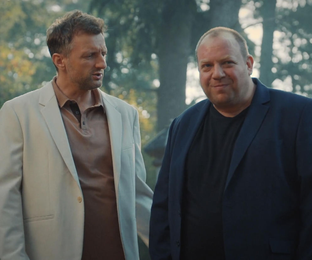 Aktorzy Bartłomiej Nowosielski jako Tadeusz i Arkadiusz Smoleński jako Bartek w scenie z odcinka M jak miłość. Bartek (po prawej w ciemnej marynarce) uśmiecha się, a Tadeusz (po lewej w beżowej marynarce) patrzy na niego z zaniepokojeniem. Więcej o ich losach na Super Seriale.