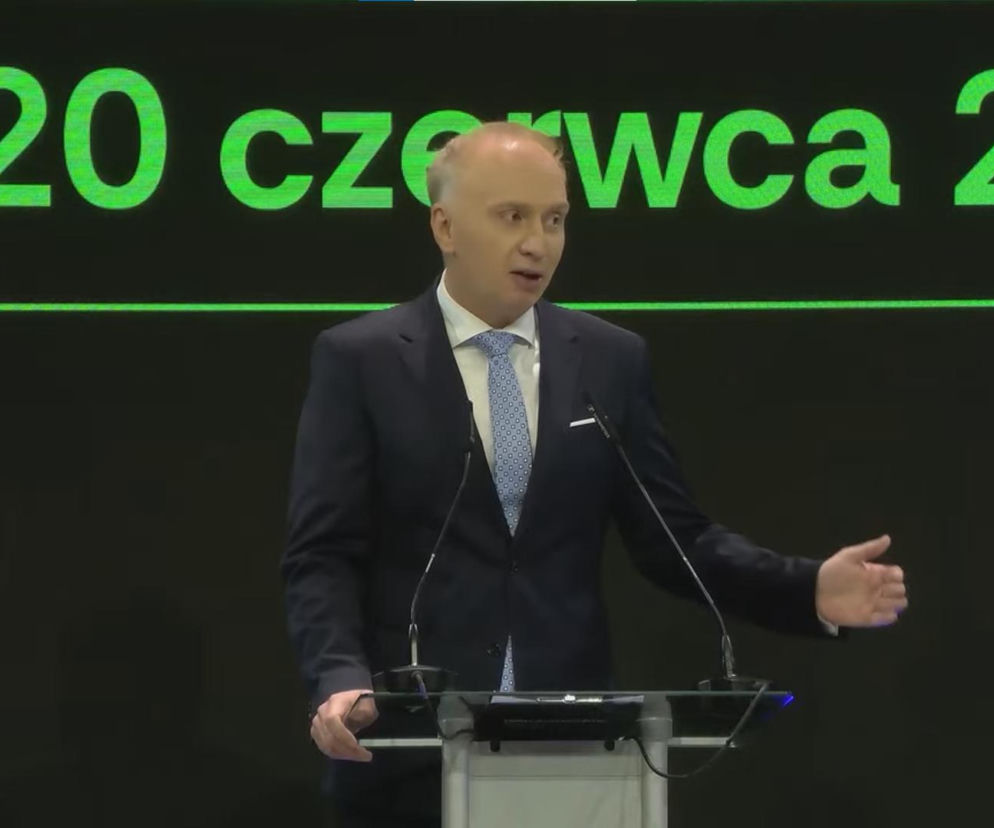 Grzegorz Zasępa, dyrektor generalny Warszawskich Targów Obronnych, w eleganckim garniturze wygłasza przemówienie na tle zielonego napisu z datą 19-20 czerwca 2026, gestykulując w trakcie prezentacji. Więcej o wydarzeniu przeczytasz na naszym portalu.