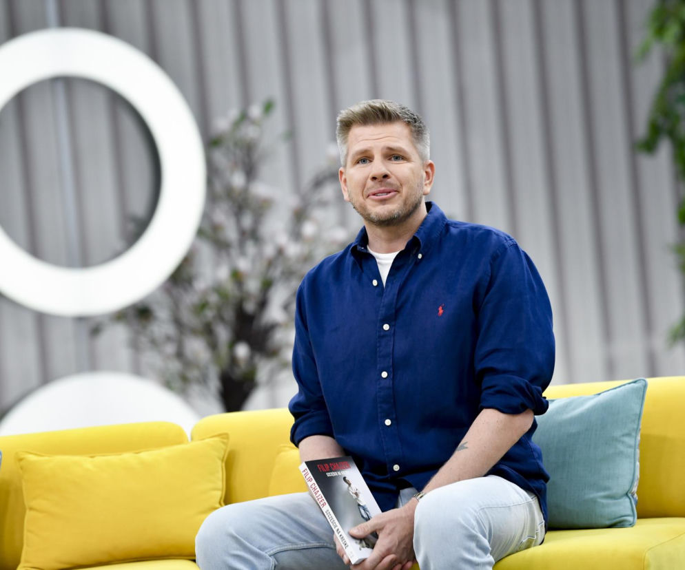 Filip Chajzer siedzi na żółtej kanapie i trzyma swoją książkę. O jego nowej willi w Krakowie przeczytasz na Eska.