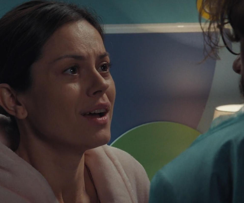 Kasia (Paulina Lasota) z serialu M jak miłość w jasnoróżowym szlafroku, z rozpuszczonymi włosami, rozmawia z Jakubem (Krzysztof Kwiatkowski), którego widać z tyłu, w niebieskiej koszuli. Ich rozmowa dotyczy narodzin dziecka. Więcej o ich losach na stronie Super Seriale.