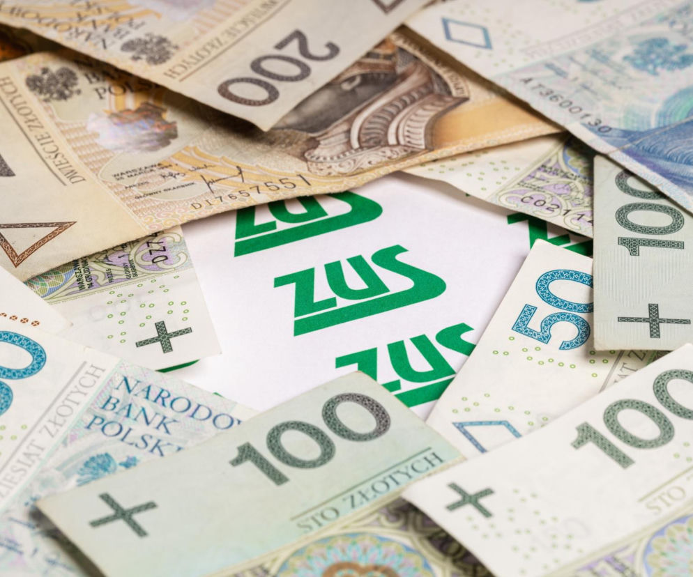 Banknoty 50, 100 i 200 złotowe rozsypane wokół białej kartki z zielonym napisem ZUS. Obraz symbolizuje oszczędności i Mały ZUS Plus, omawiane na portalu Super Biznes, wskazując na kluczowe zmiany od 2026 roku i sposoby na obniżenie składek.