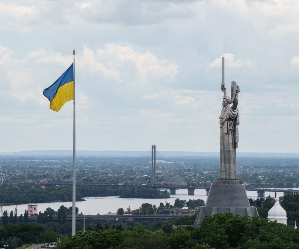 Ukraińska flaga narodowa oraz monumentalny posąg Matki Ojczyzny w Kijowie na tle rzeki Dniepr i miejskiego krajobrazu. Na naszym portalu przeczytasz o badaniach KMIS dotyczących stosunku Ukraińców do Polski.