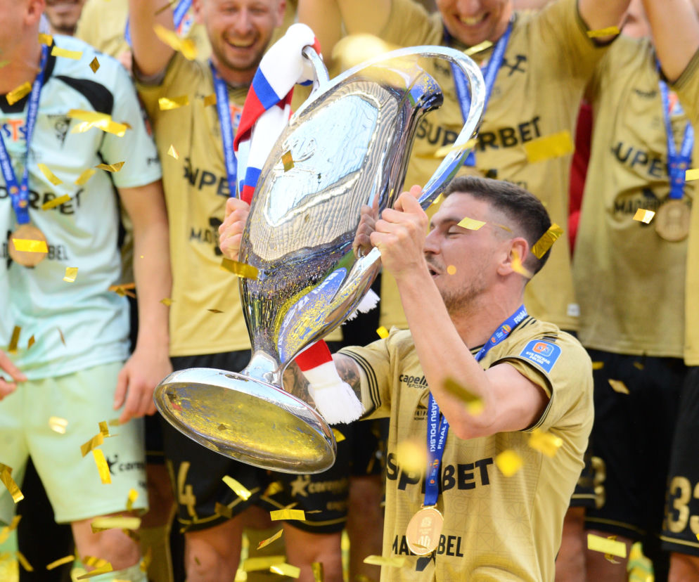 Piłkarz w złotej koszulce całuje puchar wśród kolegów z drużyny i konfetti. O Pucharze Polski czytaj na SE Supersport.