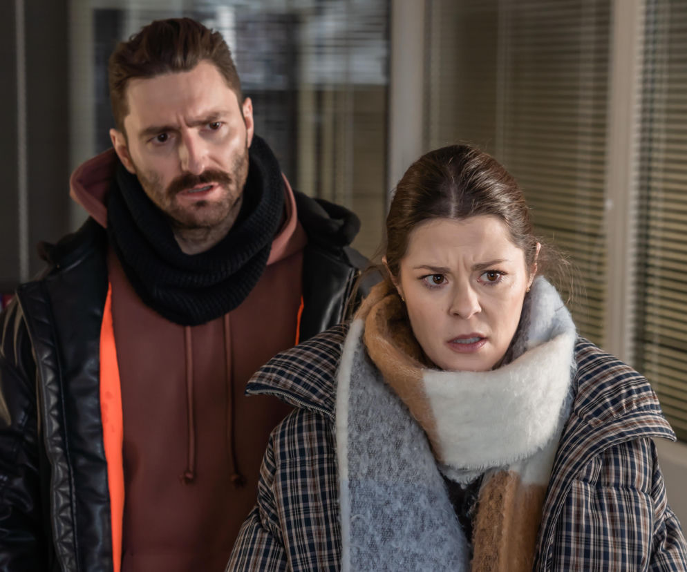 Kobieta w grubym szaliku i kraciastej kurtce oraz mężczyzna z brodą i w czarnym szaliku spoglądają z zaniepokojeniem w prawo, w tle widoczne są puste pomieszczenia. To kadr z serialu Sprawiedliwi. Trójmiasto, który znajdziesz na Super Seriale.