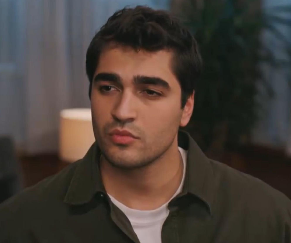 Mert Ramazan Demir jako Ferit Korhan, zamyślony w ciemnej koszuli, z krótkimi włosami, w kadrze z serialu „Złoty chłopak”. Więcej o losach Ferita przeczytasz na Super Seriale.