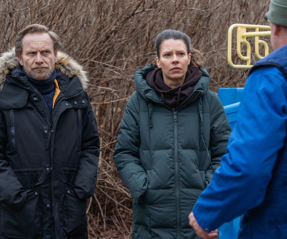 Kamil Szklany jako Maksym Pietras i Angelika Kurowska jako Patrycja Berg, stojący na zewnątrz w ciepłych kurtkach, słuchają osoby w niebieskiej kurtce, odwróconej plecami. Detektywi z serialu Sprawiedliwi. Trójmiasto rozwiązują kryminalną zagadkę. Więcej o ich przygodach na portalu Super Seriale.