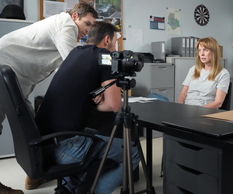 Agnieszka (Katarzyna Tlałka) siedząca przy biurku w szarej koszulce, przesłuchiwana przez dwóch policjantów (Oskar Stoczyński i Łukasz Borowski). Obok nich kamera nagrywa zeznania. Kobieta wyprze się porwania Łukasza i będzie robić z siebie ofiarę, co jest tematem na Super Seriale.