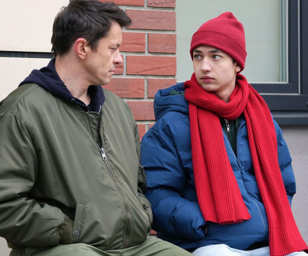Daniel (Marcin Bikowski) i Emil (Artem Malaszczuk) z serialu Barwy szczęścia w kurtkach, siedzący na zewnątrz. Daniel wpatruje się w Emila, który ma na sobie czerwoną czapkę i szalik. Scena z 3373 odcinka, gdzie Daniel udziela Emilowi męskich rad. Więcej o Super Seriale znajdziesz na naszym portalu.