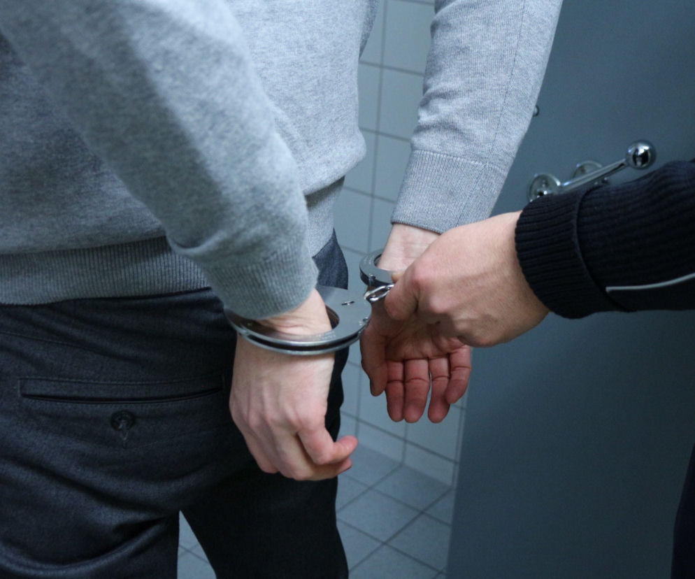 Dłonie policjanta zakładającego kajdanki na ręce mężczyzny. O wyroku za handel narkotykami przeczytasz na Eska Tarnów.
