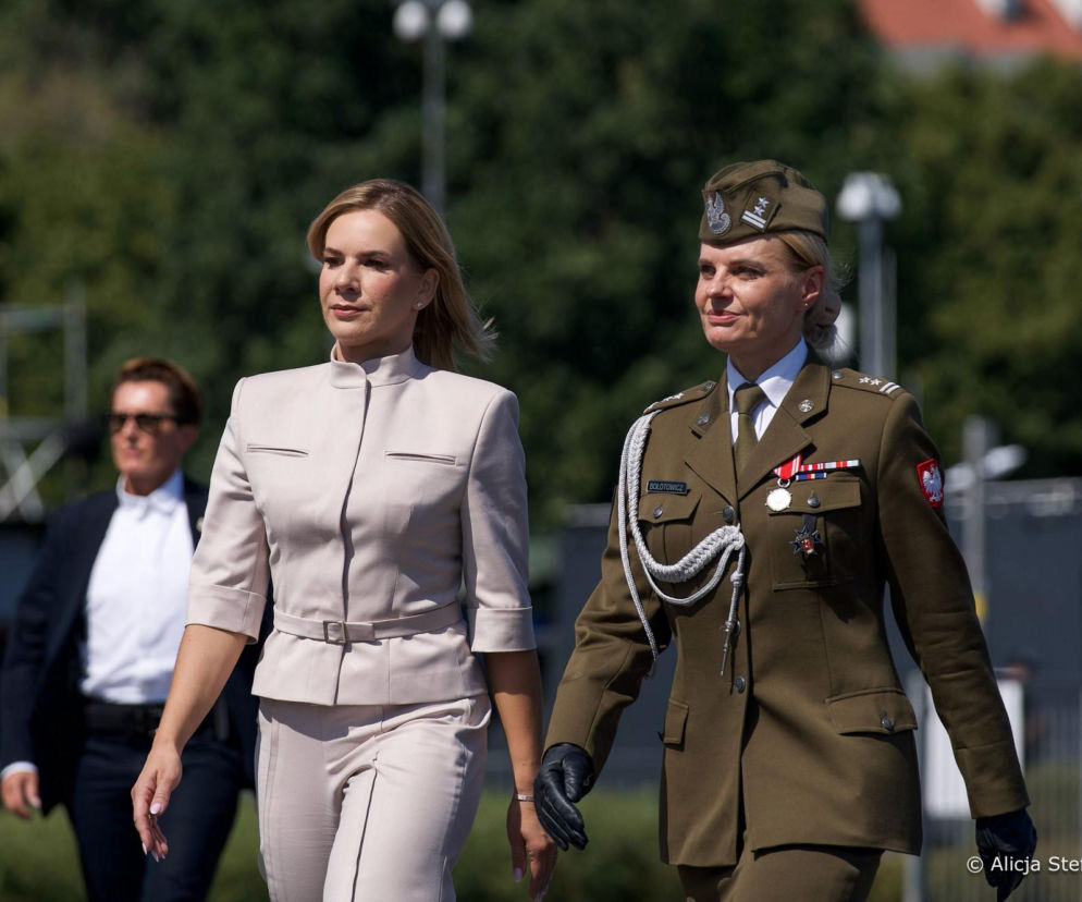 Marta Nawrocka w jasnym kostiumie idzie obok żołnierki podczas Święta Wojska Polskiego. O szczegółach przeczytasz na SE.