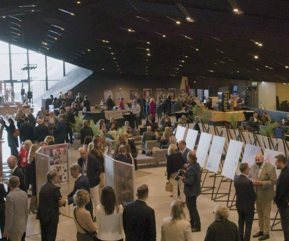 Uczestnicy XI Kongresu Wyzwań Zdrowotnych podczas przerw kuluarowych, dyskutujący w nowoczesnej przestrzeni eventowej. Na pierwszym planie widoczne stoiska z grafikami, zaś w tle panoramiczne okna i oświetlenie. O dezinformacji zdrowotnej można przeczytać na portalu Poradnik Zdrowie.