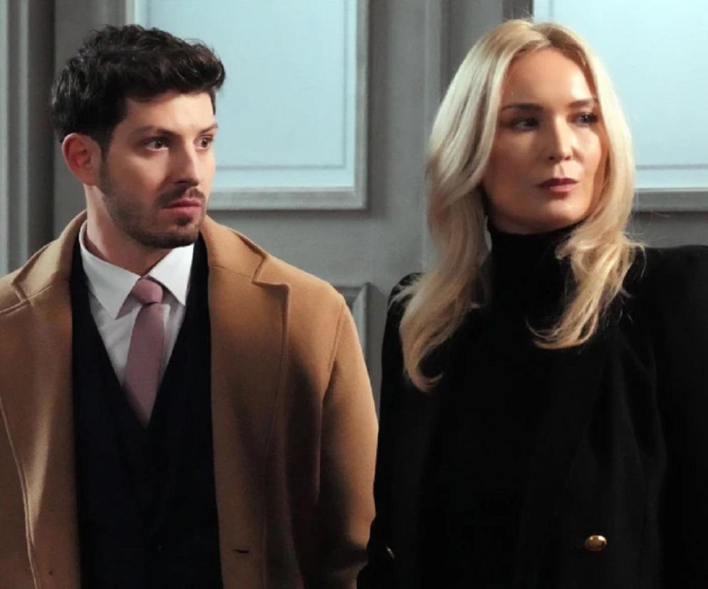 Justin (Jasper Sołtysiewicz) w beżowym płaszczu i różowym krawacie, z zaniepokojoną miną, stoi obok Karoliny (Marta Dąbrowska) w czarnym golfie i marynarce. Karolina patrzy w prawo z poważnym wyrazem twarzy. Scena z serialu Barwy szczęścia dostępna na Super Seriale.