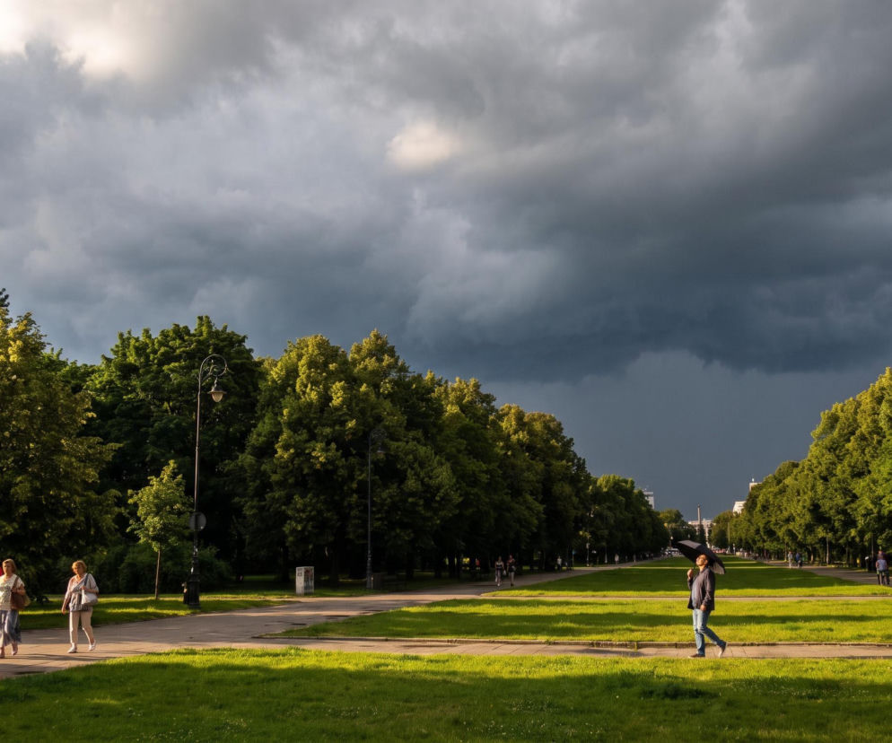 Ciemne chmury burzowe nad parkiem i spacerującymi ludźmi. O prognozie pogody na weekend przeczytasz w Eska.