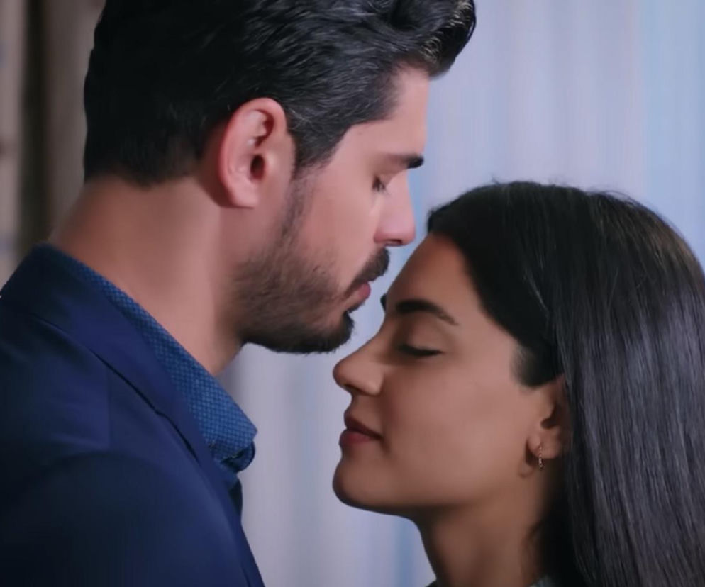 Zbliżenie na twarze Hancer i Cihana z tureckiego serialu Panna młoda w romantycznej scenie przed pocałunkiem. Mężczyzna z ciemnym zarostem delikatnie pochyla się nad kobietą o długich, ciemnych włosach. Oboje mają zamknięte oczy, co symbolizuje intymność ich pierwszej nocy, o której można przeczytać na Super Seriale.