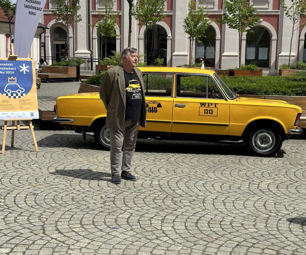 Mężczyzna przy żółtej taksówce i plakacie konkursu Poznański Taksówkarz Roku. O plebiscycie przeczytasz w Eska Poznań.