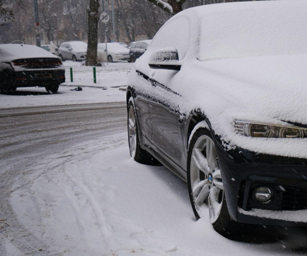Ciemny samochód zasypany warstwą śniegu na parkingu w mieście. O ataku zimy przeczytasz na SE Pogoda.