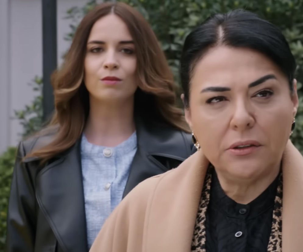 Kobieta z ciemnymi włosami w beżowym płaszczu i czarnej bluzce z panterkowym wzorem rozmawia z drugą kobietą o długich, brązowych włosach, ubraną w jasnoniebieską bluzkę i czarną kurtkę, która ma wyraźnie poważną minę. To kadr z serialu „Panna młoda” i możesz o tym przeczytać na Super Seriale.