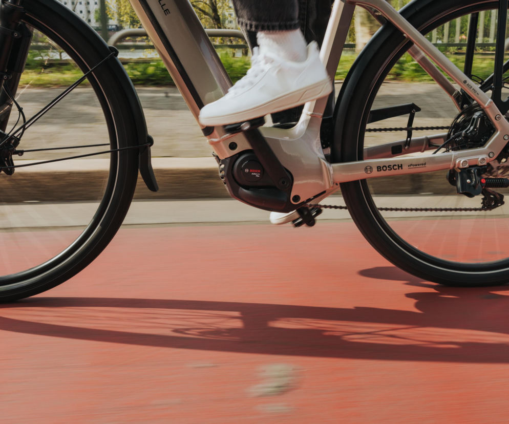 Szary e-rower Bosch z widocznym napędem Hub Line, w ruchu na czerwonej ścieżce rowerowej. Obraz z dynamicznym rozmyciem ruchu podkreśla innowacyjność nowego silnika i akumulatora Bosch eBike Systems, o czym przeczytasz na Super Biznes.