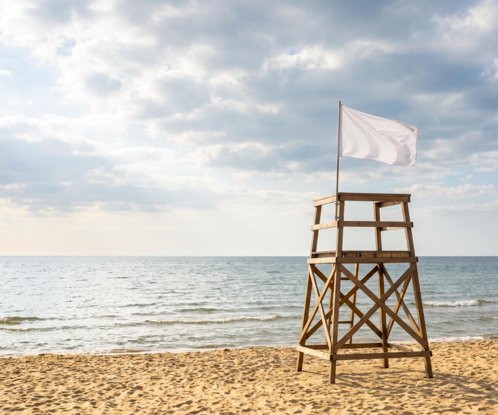 Biała flaga na wieży ratowniczej na plaży w Mrzeżynie. O bezpiecznej kąpieli bez sinic przeczytasz na SE Szczecin.