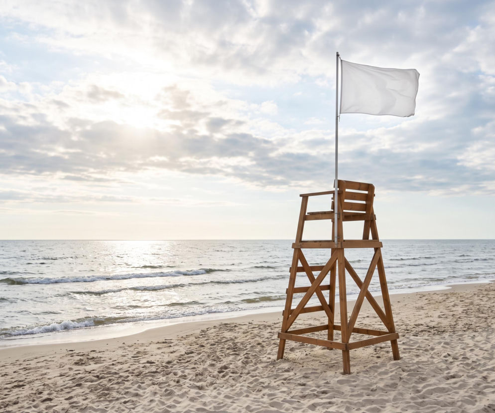 Drewniana wieża ratownika z białą flagą na pustej plaży nad morzem. O warunkach w Łazach przeczytasz na SE Szczecin.