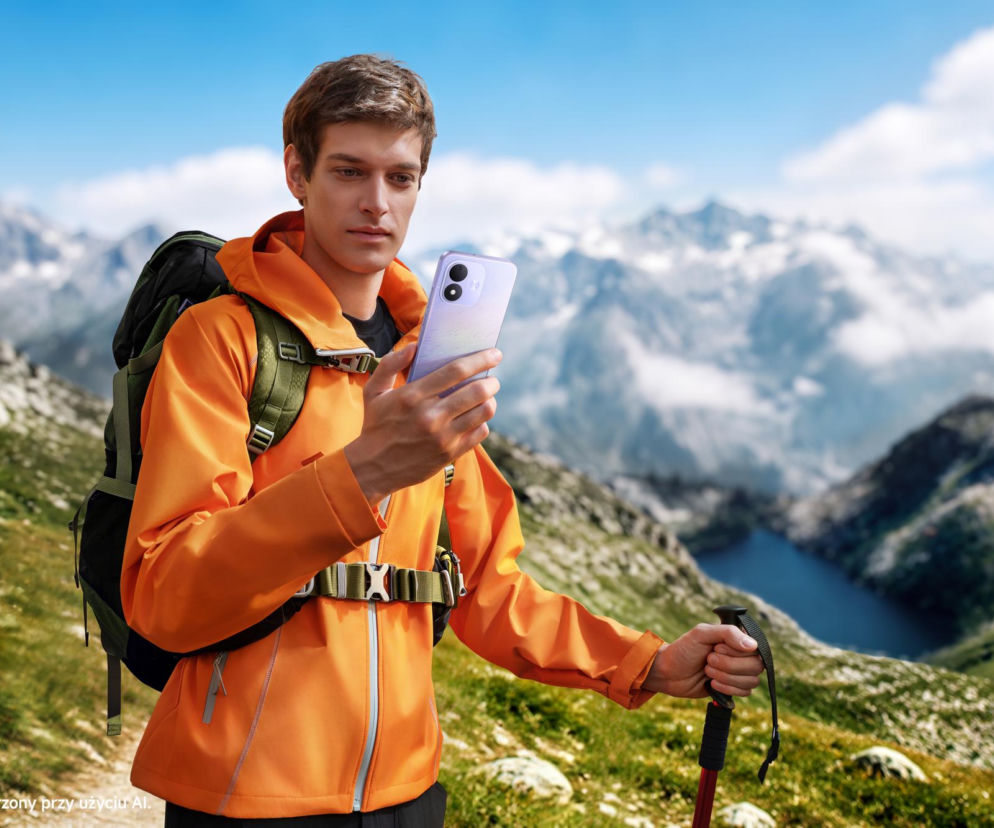 Turysta w pomarańczowej kurtce trzyma smartfon Redmi Note 17 na tle gór. O nowej serii Xiaomi przeczytasz na Eska.