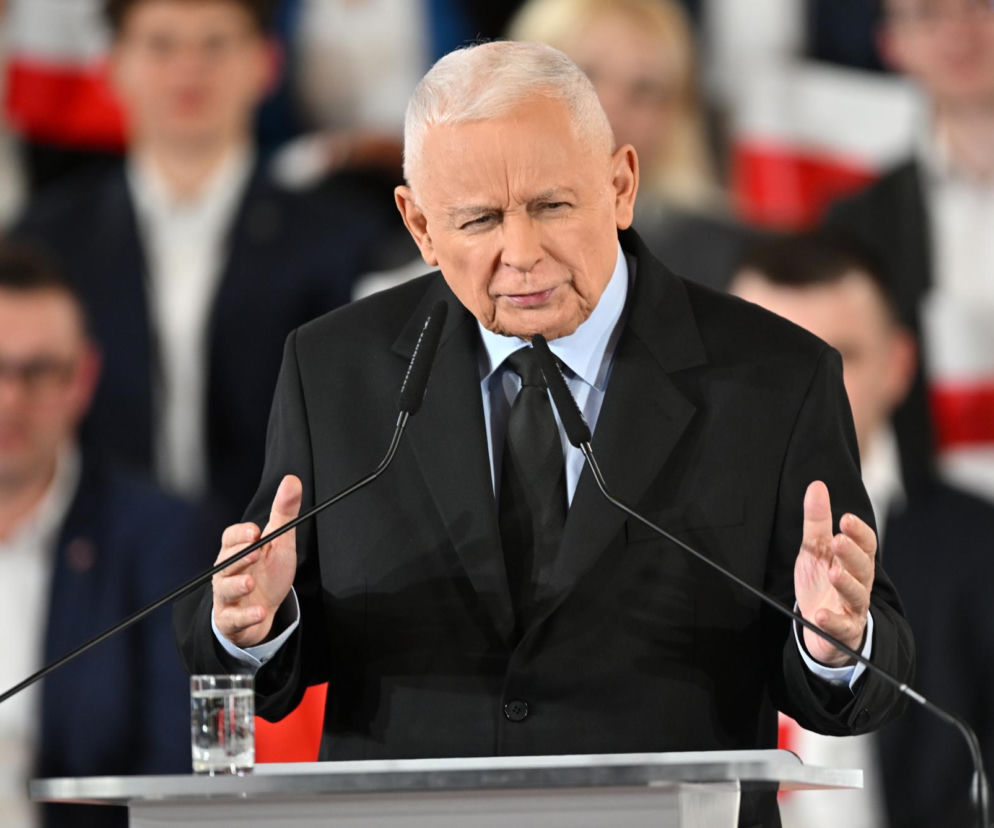 Jarosław Kaczyński, prezes PiS, przemawia za mównicą z dwoma mikrofonami, gestykulując dłońmi. Jest ubrany w ciemny garnitur i krawat. W tle rozmazana publiczność. Więcej na temat decyzji o zwrocie odznaczenia możesz przeczytać na naszym portalu.