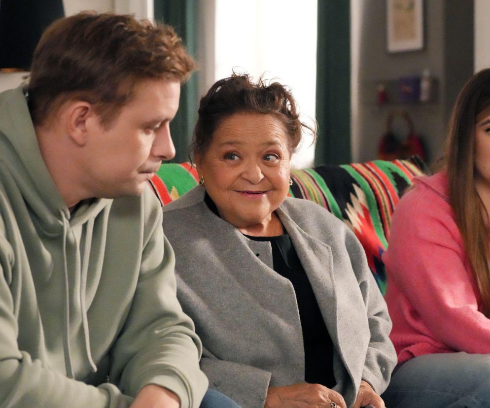 Trzy osoby, młody mężczyzna w zielonej bluzie, starsza kobieta w szarym płaszczu i młoda kobieta w różowej bluzie, siedzą na kanapie, zmartwieni sytuacją związaną z domem Pyrków. Scena z odcinka Barw szczęścia, więcej na Super Seriale.