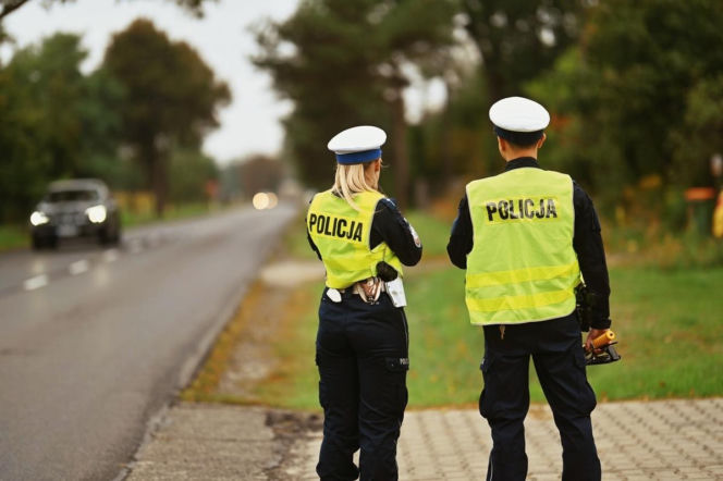 Dwoje policjantów tyłem przy drodze, w tle auto. O kontroli 14-latka pod Skierniewicami czytaj na Eska Łódź.