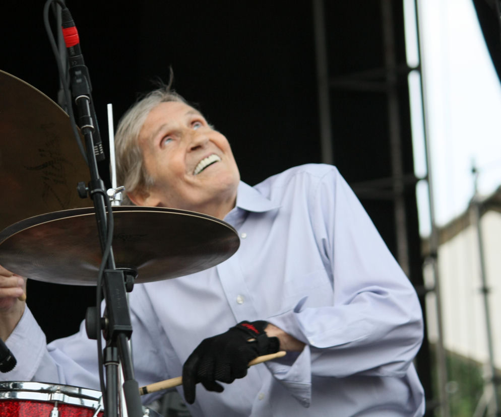 Uśmiechnięty perkusista Levon Helm z The Band gra na perkusji. O historii grupy i groupies przeczytasz na EskaRock.