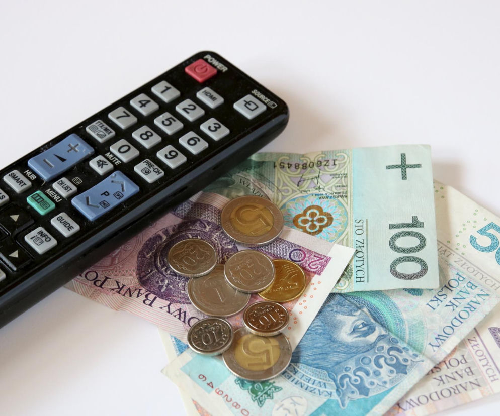 Czarny pilot do telewizora leży obok polskich banknotów i monet. O opłatach RTV przeczytasz na SE Superbiz.