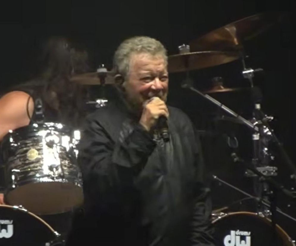 William Shatner śpiewa do mikrofonu na scenie w otoczeniu perkusji. O jego metalowym koncercie przeczytasz na EskaRock.