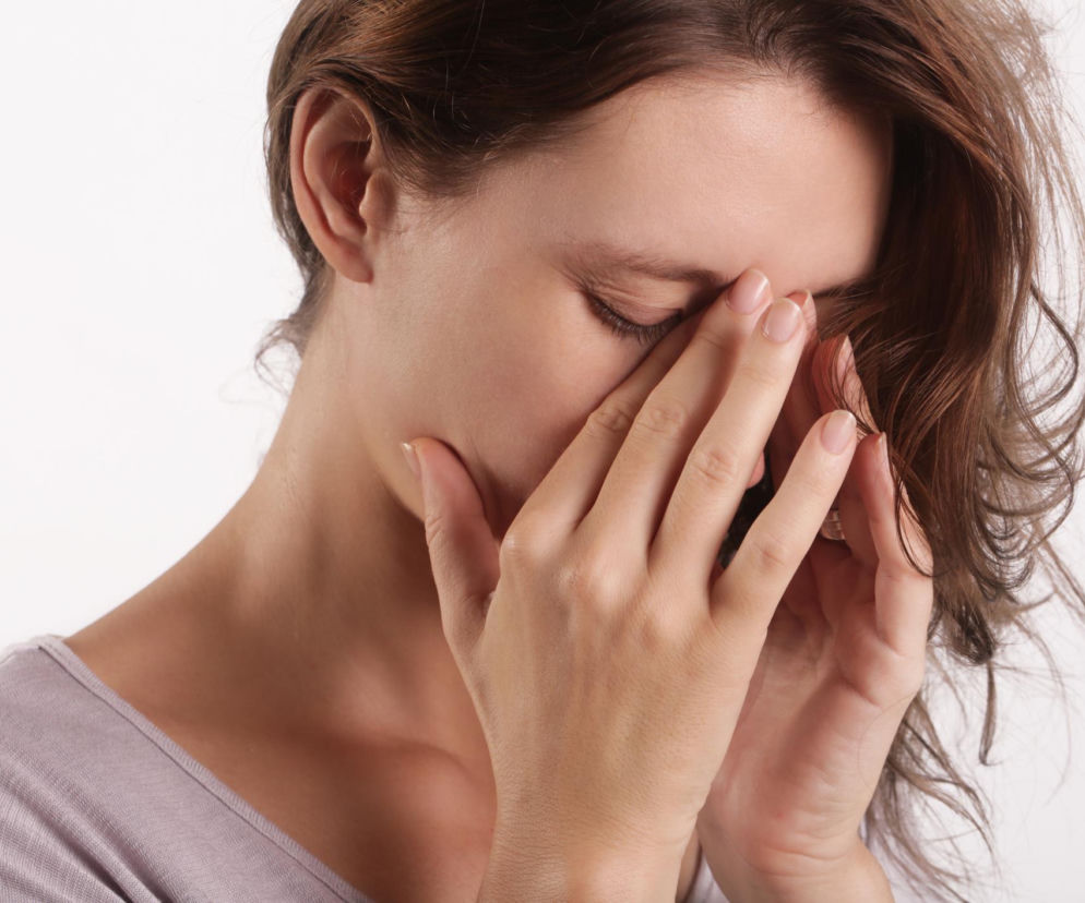 Kobieta z dłońmi na twarzy, masująca okolicę nosa i zatok, z zamkniętymi oczami, symbolizuje zmęczenie lub problemy z oddychaniem. Odczucia związane z alternatywnym zatykaniem się dziurek nosa i cyklem biologicznym nosa, o którym przeczytasz więcej na Poradnik Zdrowie.