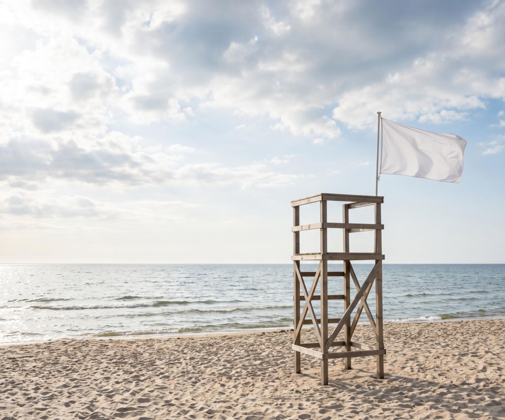 Drewniana wieża ratownicza z białą flagą na pustej plaży w Łazach. O bezpieczeństwie w wodzie przeczytasz na SE Szczecin.