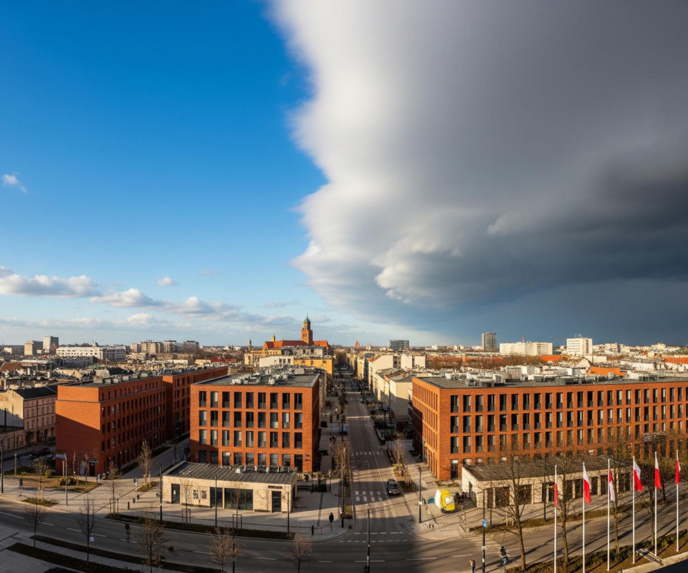 Panorama miejska ukazuje horyzont podzielony wyraźną linią pomiędzy jasnym, błękitnym niebem z pojedynczymi białymi chmurami po lewej stronie a gęstą, ciemnoszarą chmurą burzową po prawej. Poniżej rozciąga się miejski krajobraz z licznymi budynkami o różnej architekturze, w tym dominujące są nowoczesne, ceglane konstrukcje z dużą ilością okien. Ulice, częściowo zalane słońcem, a częściowo zacienione, krzyżują się, widać na nich pojazdy i pojedynczych pieszych; w prawym dolnym rogu na masztach powiewają biało-czerwone flagi.
