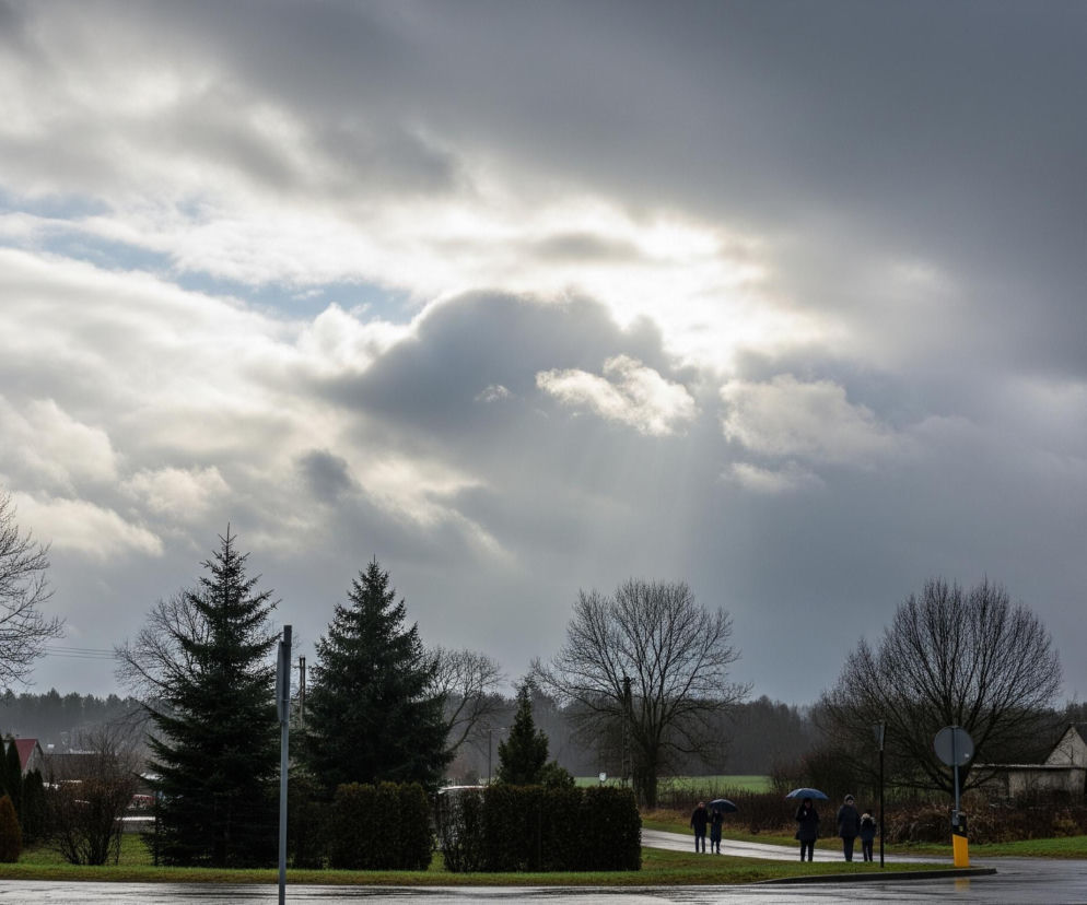 Niebo jest zdominowane przez gęste, szaro-białe chmury, z fragmentami błękitnego nieba widocznymi między nimi oraz jasnymi promieniami słońca przebijającymi się przez opóźniające się chmury w centrum kadru. Poniżej rozciąga się wiejski lub podmiejski krajobraz z licznymi drzewami o nagich gałęziach i kilkoma ciemnozielonymi iglakami, a także fragmentami zielonej trawy. Na mokrym asfalcie widoczna jest grupa ludzi w oddali oraz dwie osoby z parasolami bliżej lewego i prawego brzegu obrazu.