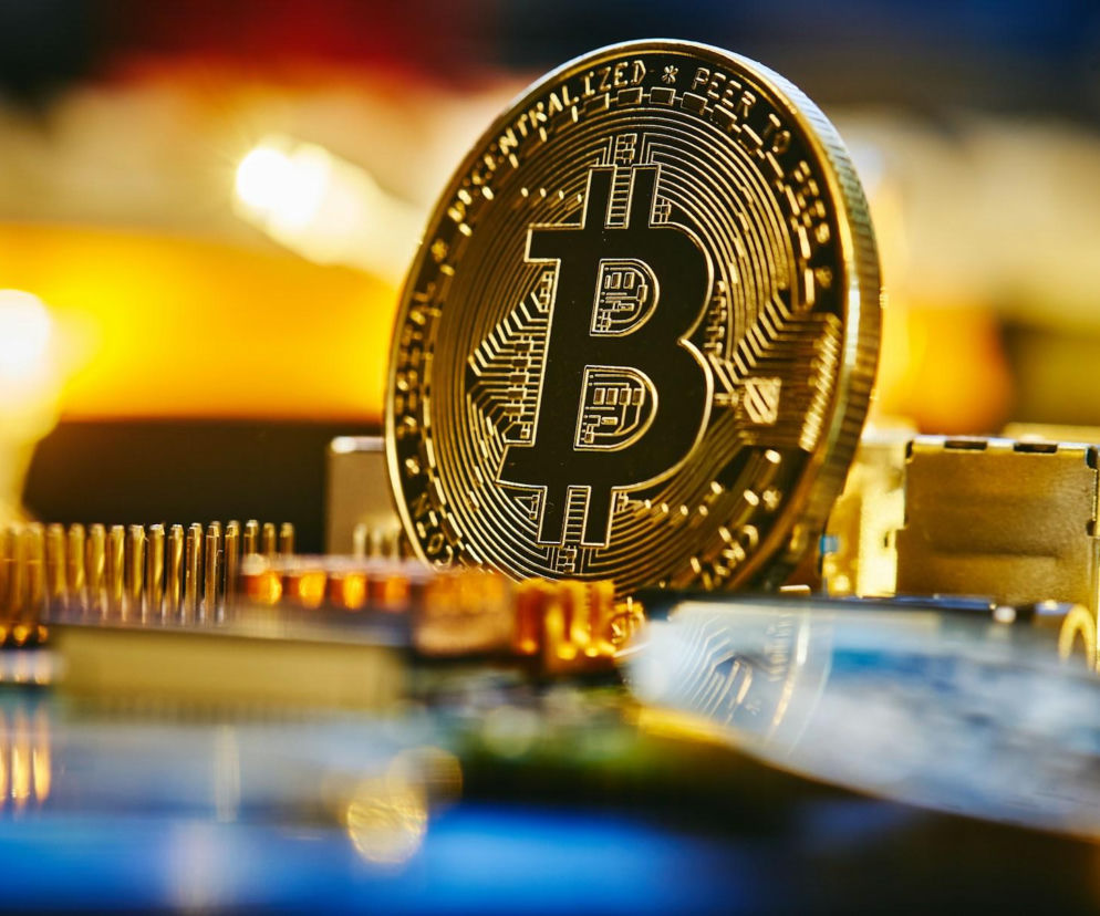 Złota moneta Bitcoin na płytce drukowanej, symbolizująca połączenie cyfrowych aktywów z technologią. Zdjęcie ilustruje temat dostępu do kryptowalut, o czym można przeczytać na Super Biznes.