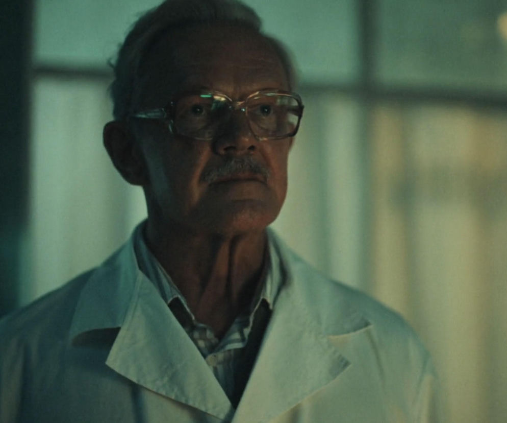 Portret aktora Cezarego Pazury jako profesora Andrzeja Zajdlera z serialu Czarna śmierć. Mężczyzna w okularach i białym kitlu, z wąsem, patrzy prosto przed siebie. Zdjęcie przedstawia atmosferę napięcia i spisku, o czym przeczytasz na stronie Super Seriale.