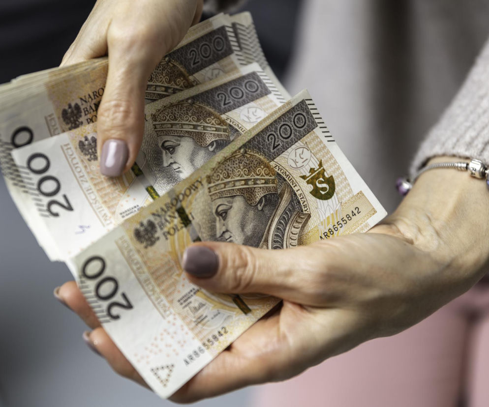 Dłonie osoby trzymające plik banknotów o nominale 200 złotych, symbolizujące emeryturę honorową ZUS dla 100-latków. O szczegółach świadczenia, które nie wymaga przepracowania ani jednego dnia, można przeczytać na portalu Poradnik Zdrowie.