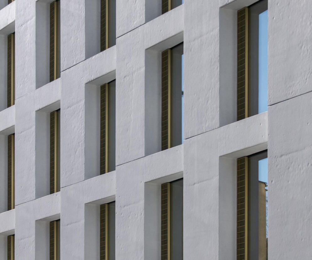 Fasada budynku biurowo-usługowego Instytutu Pileckiego przy Siennej 82 w Warszawie, z białymi, chropowatymi ścianami i regularnymi oknami w złotych ramach. Projekt autorstwa Bogumiła Kidziaka zgłoszony do konkursu Życie w Architekturze 2025, o którym przeczytasz na portalu Architektura Murator Plus.