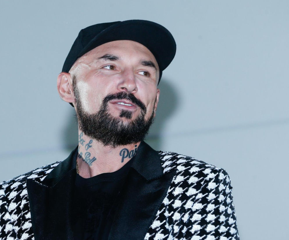 Uśmiechnięty reżyser Patryk Vega w czapce z daszkiem i wzorzystej marynarce. O jego diecie przeczytasz na SE.