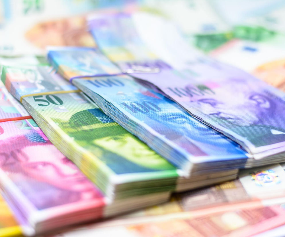 Złożone banknoty szwajcarskich franków o nominałach 20, 50 i 100, zabezpieczone gumkami, symbolizujące stabilizację i wzrost kursów walut, szczególnie franka szwajcarskiego, o czym można przeczytać na Super Biznes.