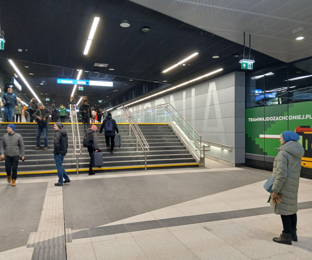 Nowoczesny tunel Dworca Zachodniego w Warszawie, ukazujący pasażerów wchodzących i schodzących po szerokich schodach. Widoczne oznakowanie kierunkowe oraz reklama „TRAMWAJDOZACHODNIEJ.PL”. Więcej o zmianach na dworcu przeczytasz na Architektura Murator Plus.
