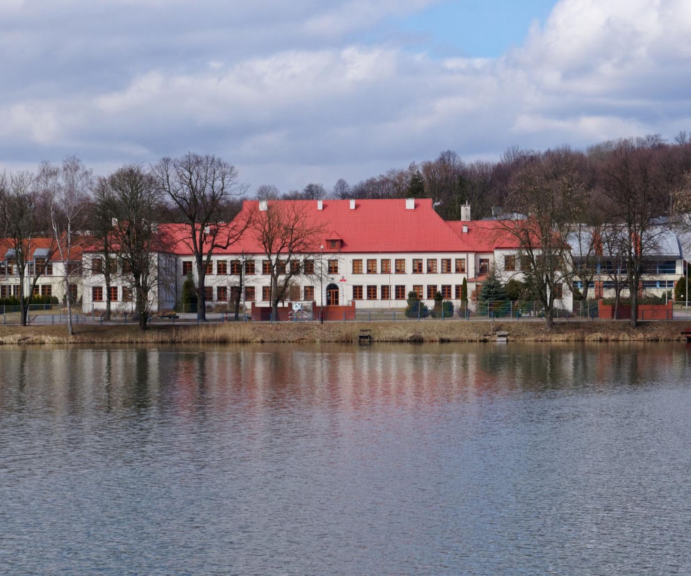 Biały budynek z czerwonym dachem nad brzegiem wody w Pilicy. O urokach tego miasta przeczytasz na Eska Śląskie.