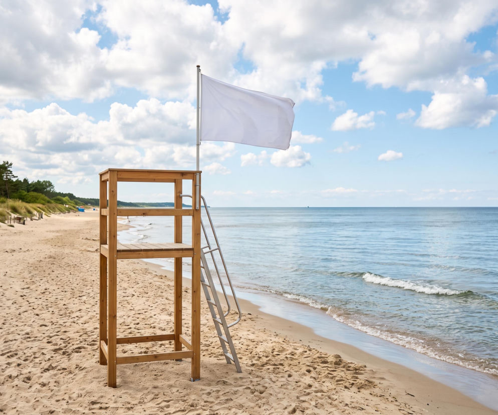 Drewniana wieża ratownicza z białą flagą na pustej plaży. O bezpieczeństwie kąpieli w Ustroniu Morskim informuje SE Szczecin.