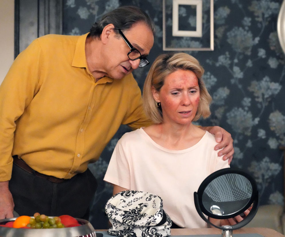 Aktor Bronisław Wrocławski jako Jerzy pociesza Joannę Gleń w roli Malwiny, której twarz jest pokryta czerwonymi plamami po nieudanym zabiegu kosmetycznym. Malwina, siedząc przy stole z lusterkiem, patrzy na swoje podrażnione czoło i policzki, podczas gdy Jerzy obejmuje ją ramieniem. To dramatyczna scena z serialu Barwy szczęścia, a więcej o niej przeczytasz na portalu Super Seriale.