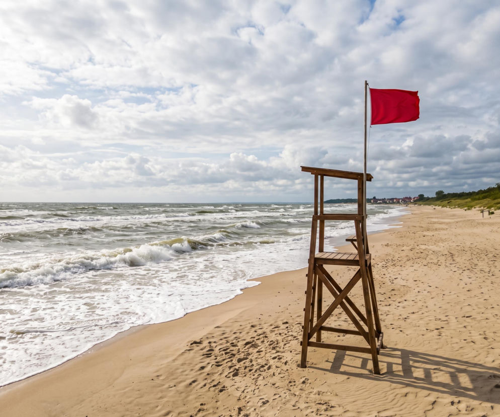 Czerwona flaga na wieży ratowniczej przy pustej plaży w Mielnie. O zakazie kąpieli przeczytasz na SE Szczecin.