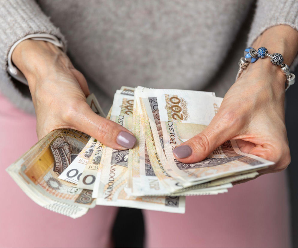 Dłonie kobiety trzymającej plik banknotów o nominale 200 złotych. O ulgach podatkowych od darowizn przeczytasz w Eska.